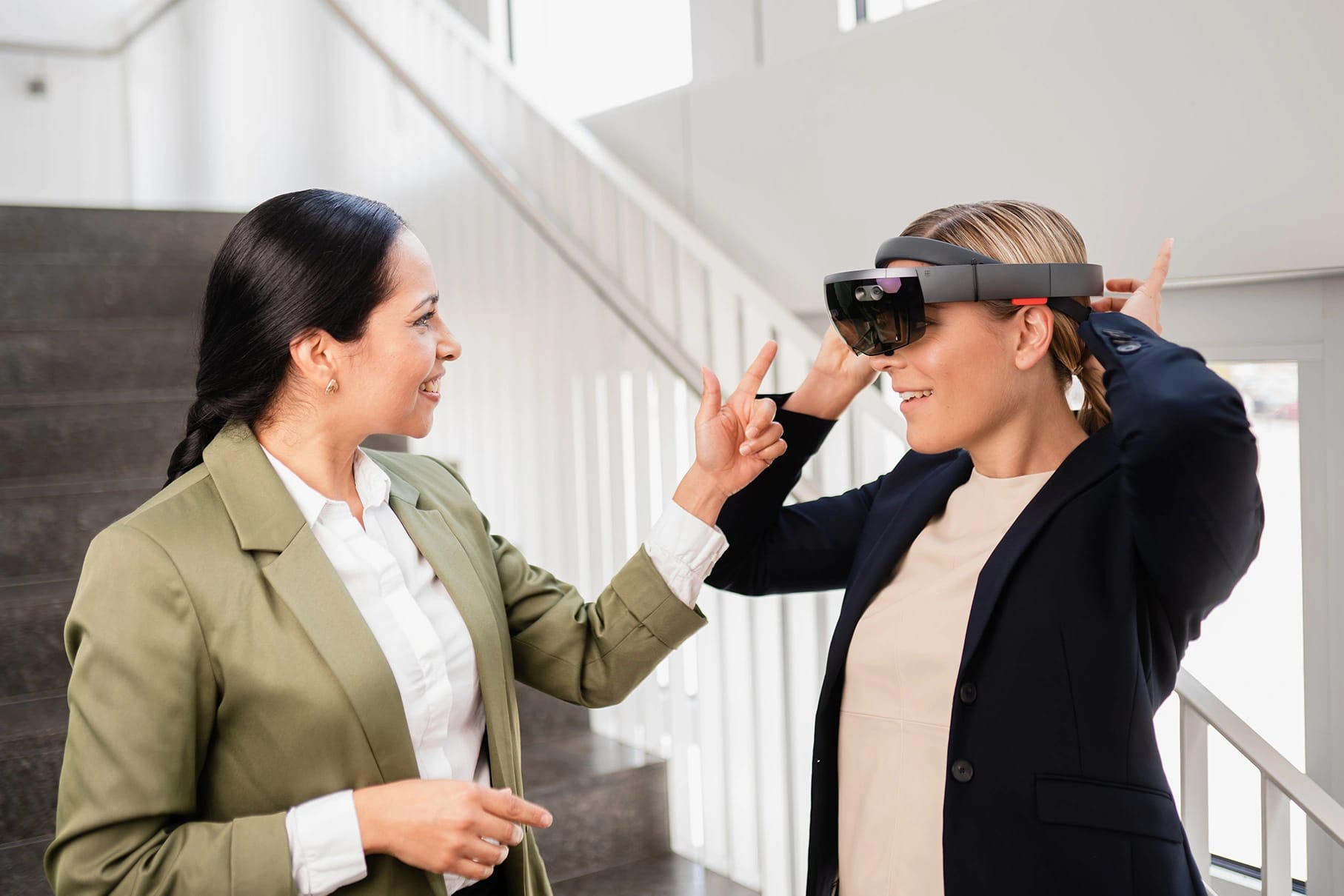 Zwei Kolleginnen unterhalten sich auf einer Treppe, während eine von ihnen eine Mixed-Reality-Brille aufsetzt.